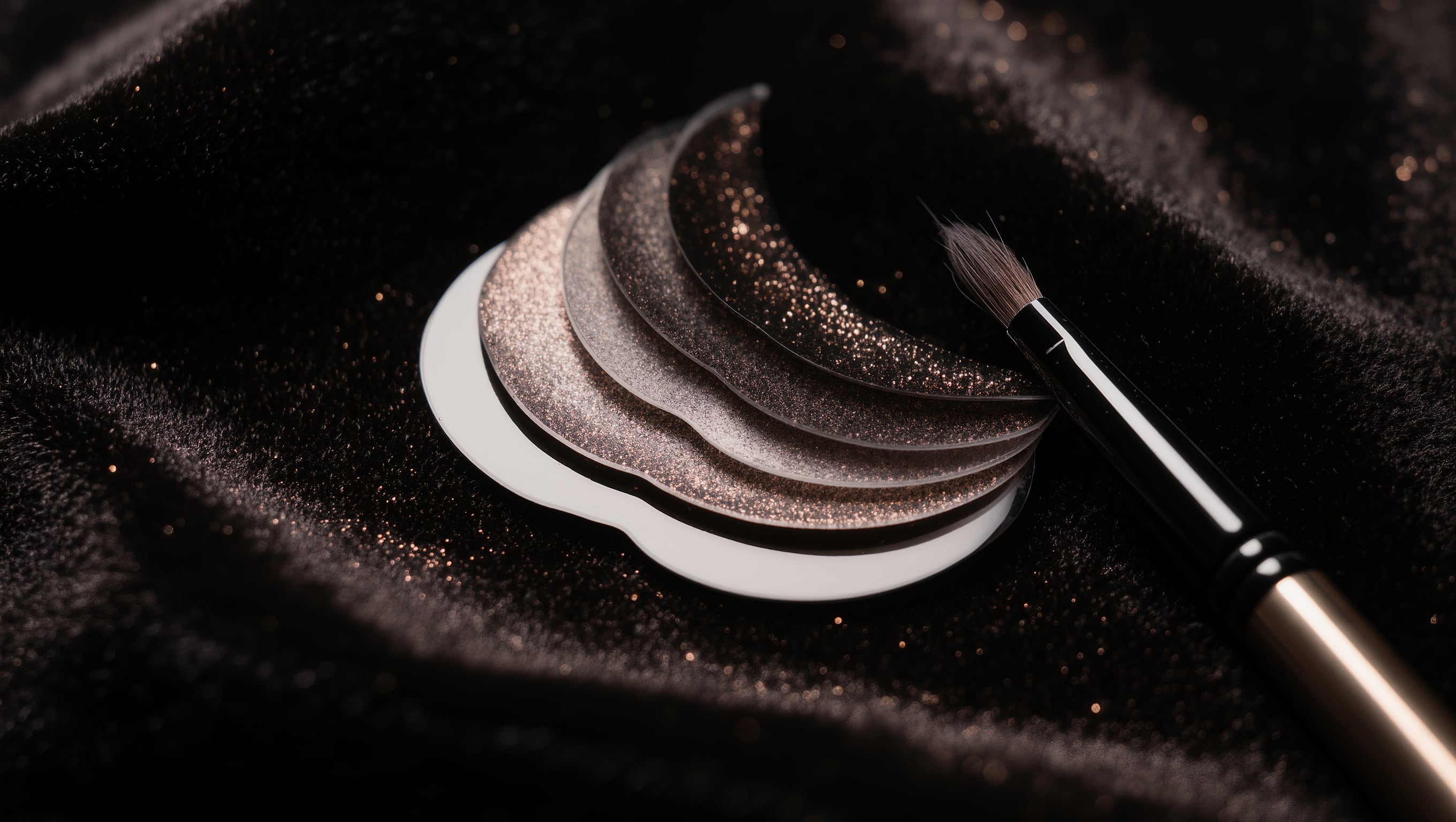 Silikonpads in verschiedenen Größen und ein feiner Applikatorpinsel liegen auf schwarzem Samt im schmalen Lichtstreifen