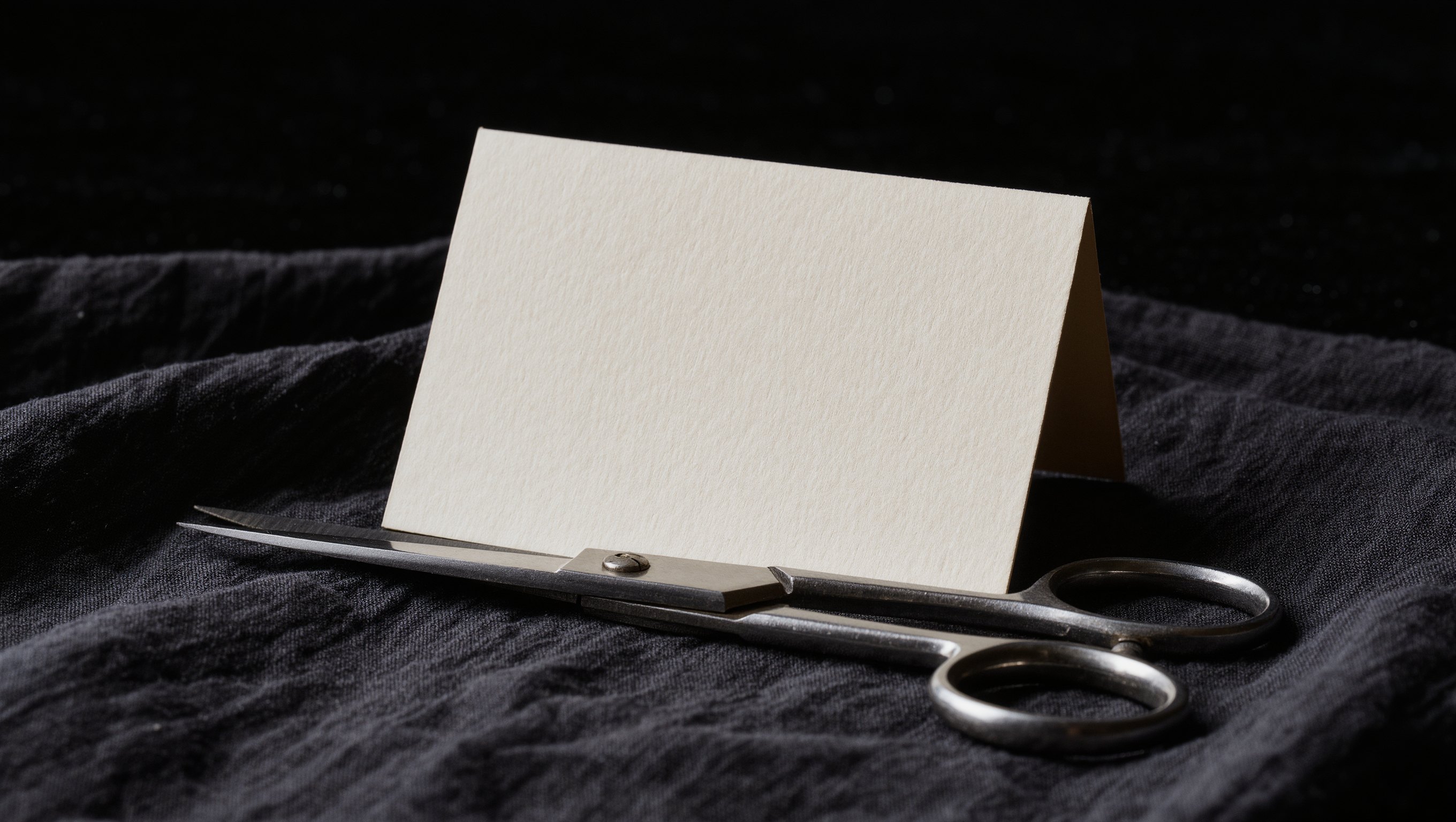 Eine aufgeschlagene Preisliste liegt unscharf im Hintergrund, im Vordergrund eine Schere und ein Farbpinsel auf dunklem Tuch